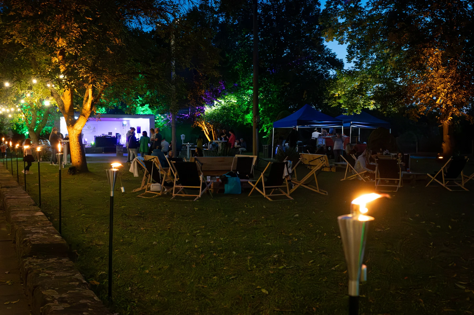 Der Garten am Abend mit Fackeln, Sitzplätzen und beleuchtetem Veranstaltungsraum
